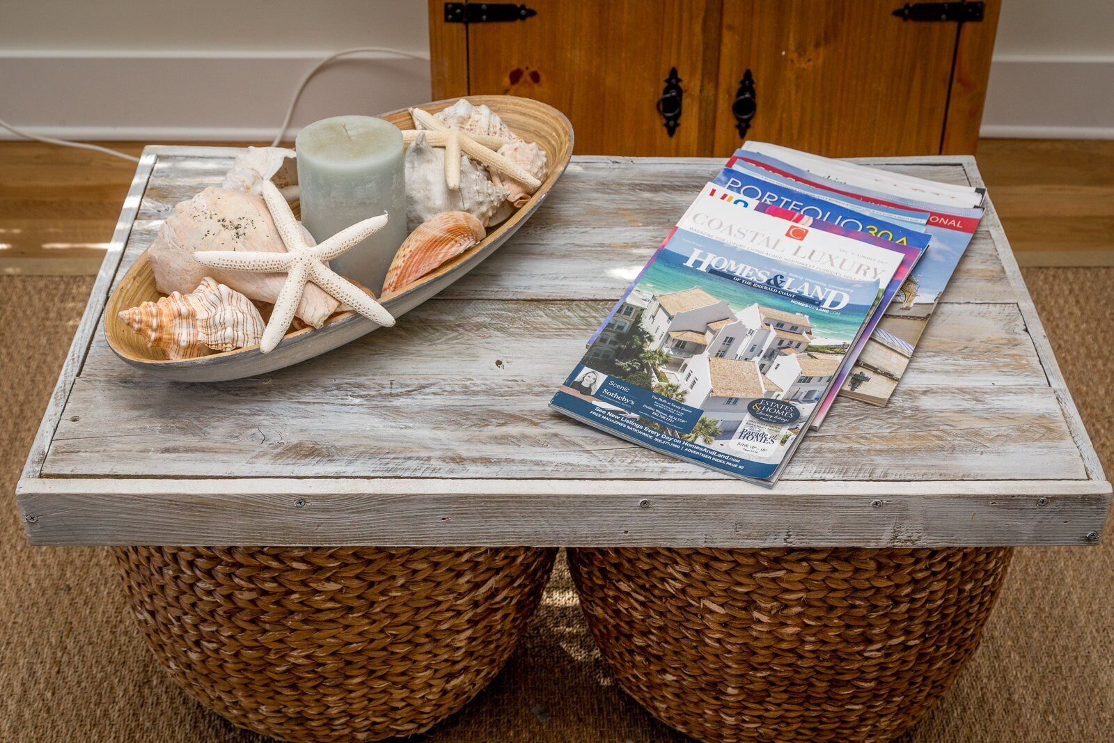 Una mesa de madera con un cuenco de conchas marinas, una vela y una revista.