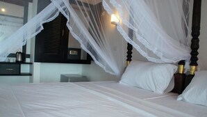 A neatly made bed with white linens and a canopy, a bedside table with a kettle, and a wall-mounted light fixture. - Hotel Ritas & Beach Restaurant (Hikkaduwa)