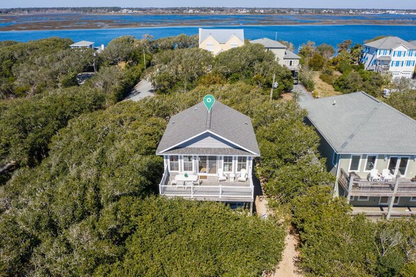 A coastal house with a large porch, surrounded by dense vegetation and a view of the ocean.