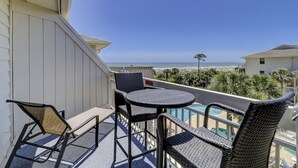 Un balcón con muebles de mimbre, piscina y vista a la playa y al océano.