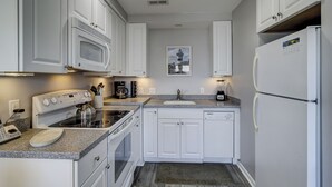 Una cocina compacta con armarios blancos, un microondas integrado, estufa, lavaplatos y refrigerador.