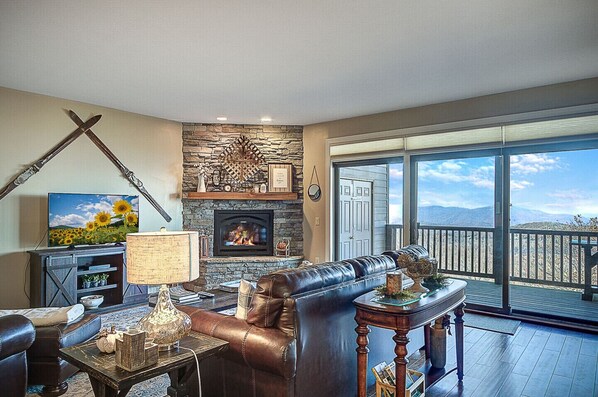 A living room with a stone fireplace, leather sofa, and a television displaying a sunflower scene.