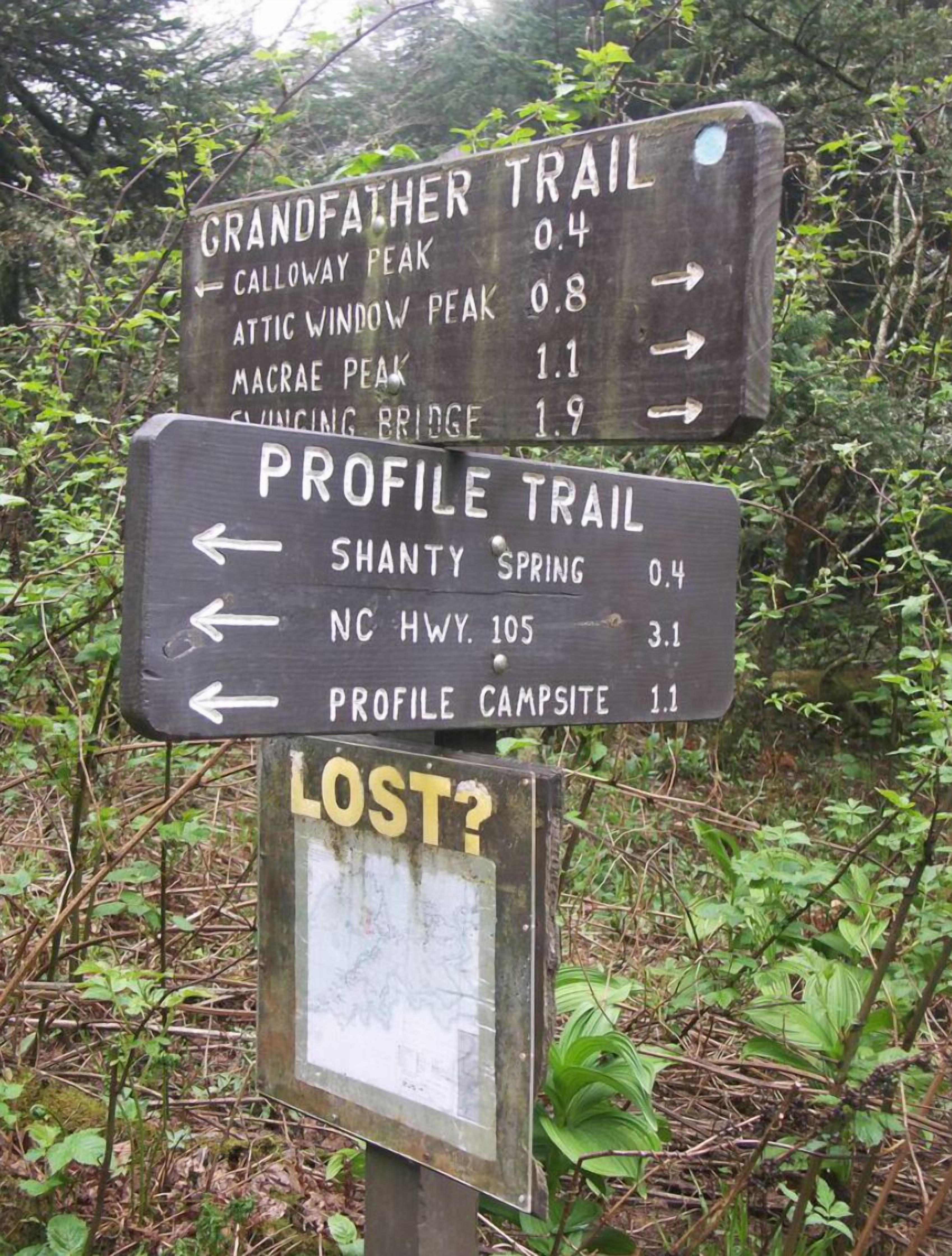 Un cartel de senderismo con indicaciones hacia diferentes cumbres y campamentos, incluyendo el sendero Grandfather y el sendero Profile.