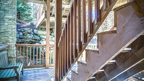 Una escalera de madera con un muro de piedra y una terraza de madera con un banco.