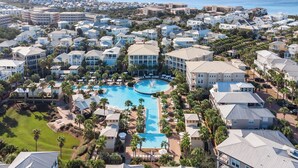 An aerial view of a resort with multiple buildings, a central swimming pool, and palm trees. - Seacrest's Forever & Always + Pool, Tram & Bikes (Seacrest)