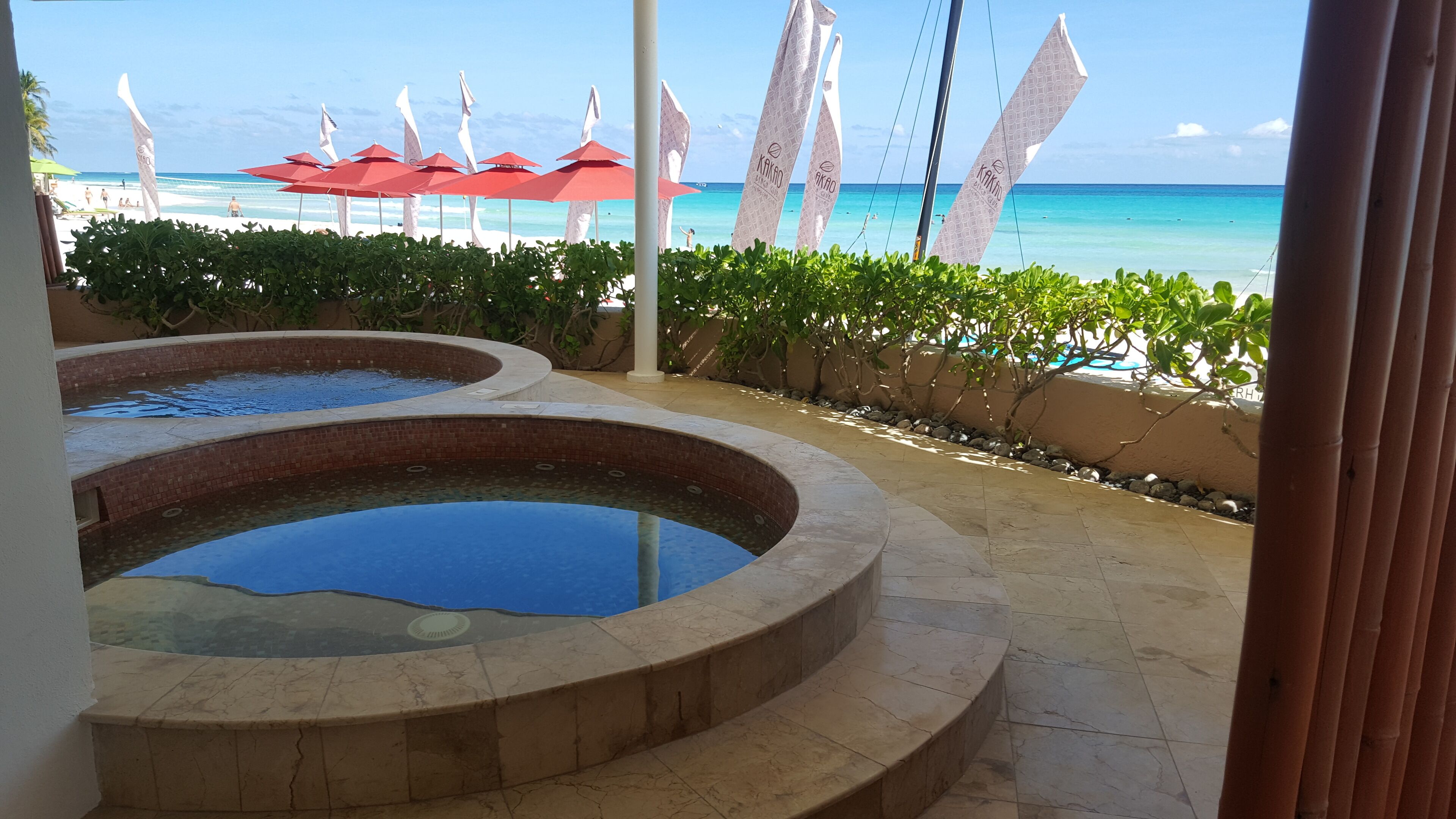Un espace piscine comprenant deux piscines rondes, entourées d’un petit muret et bordé d’une rangée de parasols rouges.