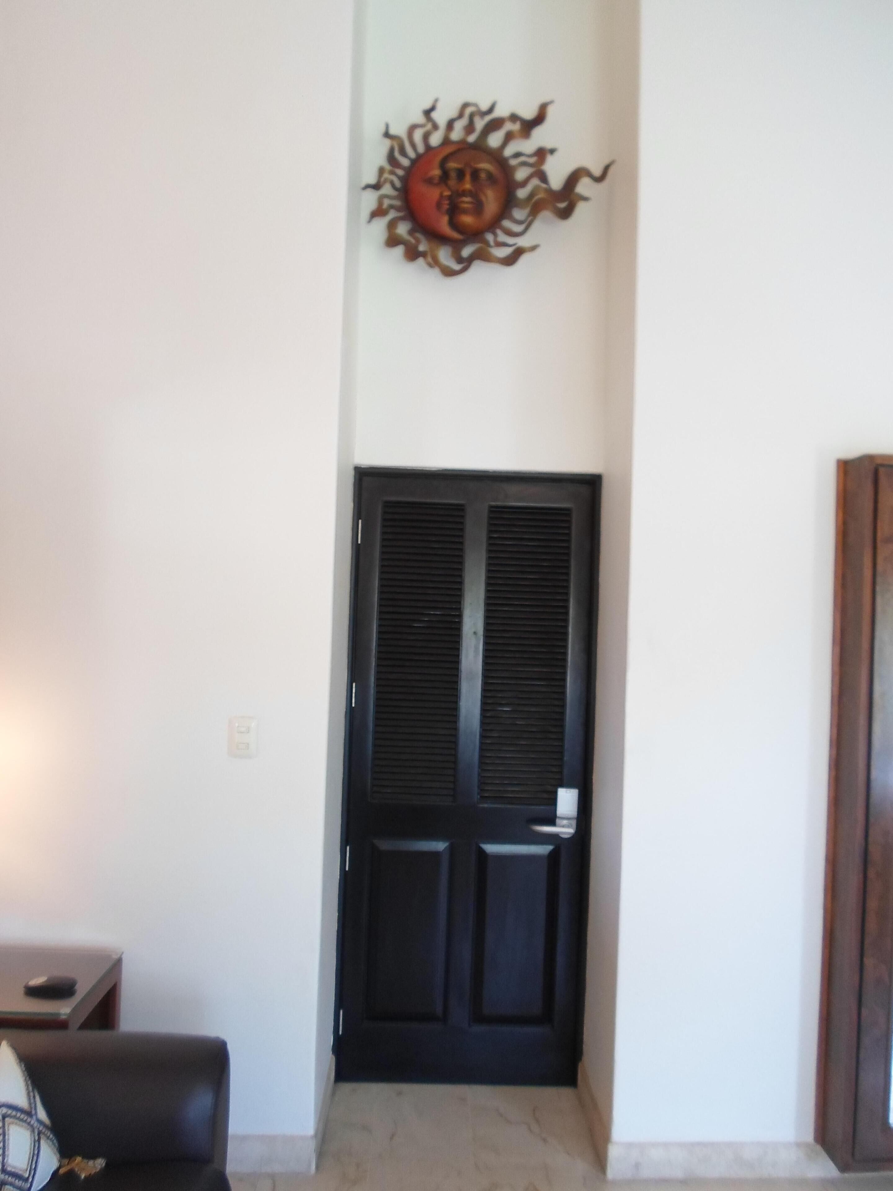 A room with a black door, a wall-mounted decorative sun, and a small table with a chair.