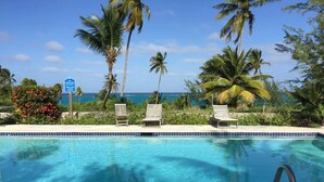 A pool with clear blue water, surrounded by palm trees and a sign indicating a lifeguard on duty. - Beautiful Hibiscus House (Governor's Harbour)