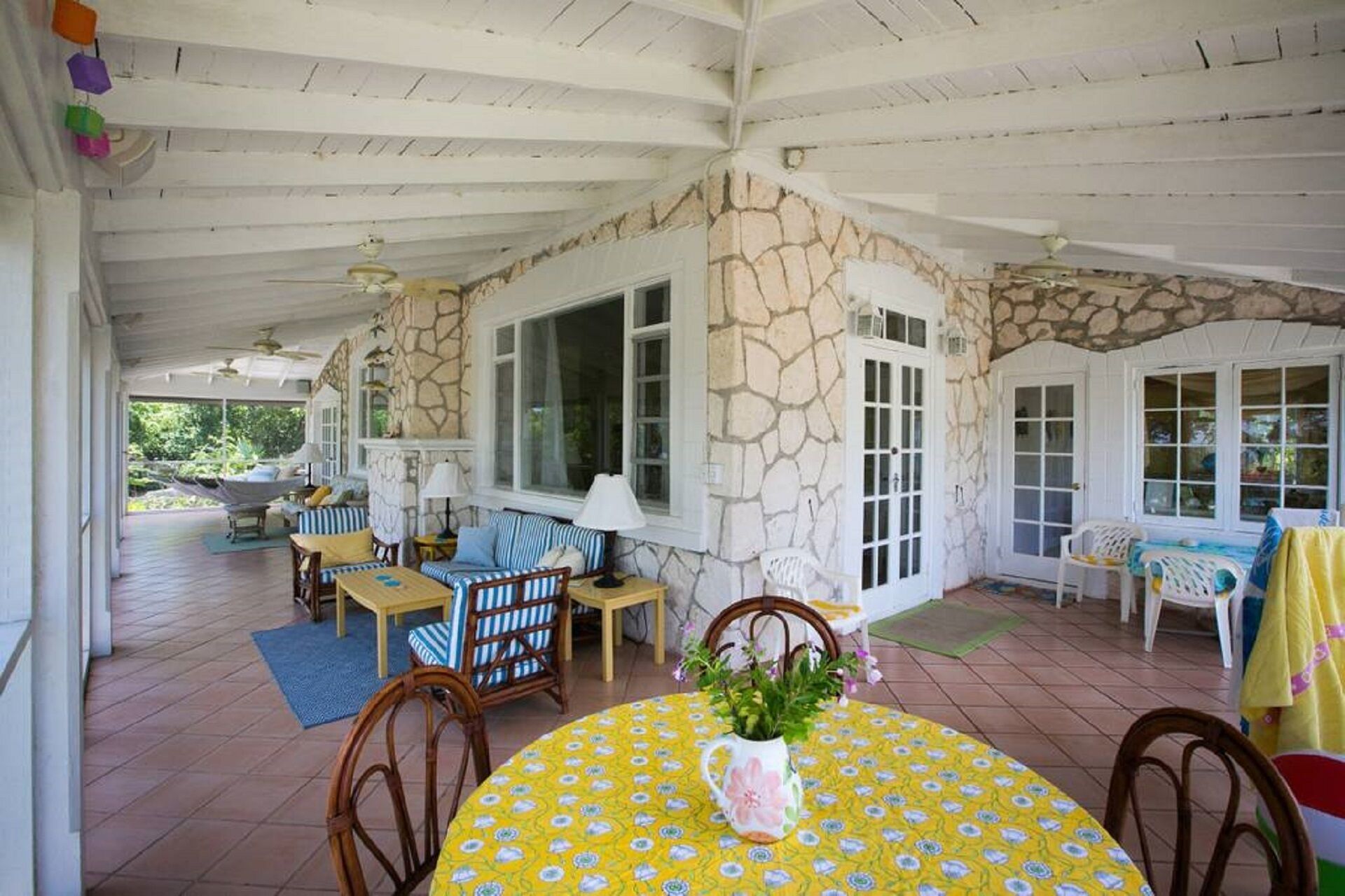 A covered patio area with stone walls, large windows, and outdoor furniture.