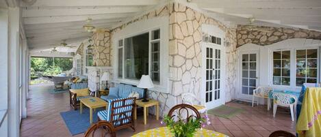 A covered patio area with stone walls, large windows, and outdoor furniture.