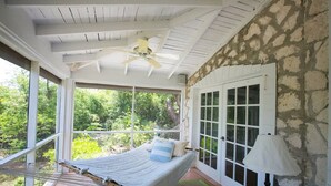 A bedroom with a bed, a hammock, a lamp, and a view of greenery. - Beautiful Hibiscus House (Governor's Harbour)