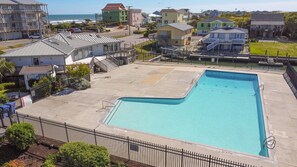 Una piscina de borde curvo, rodeada por una valla, y contigua a un edificio con una escalera que lleva a un balcón.