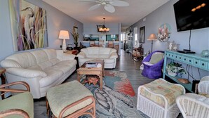 A spacious living room with a sofa, armchairs, a coffee table, and a dining area in the background. - Oceanfront 2-bedroom Queen's Grant Condo (Topsail Beach)