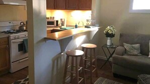 Una cocina compacta con armarios de madera, una estufa y un microondas. Hay dos taburetes cerca de la isla de la cocina.
