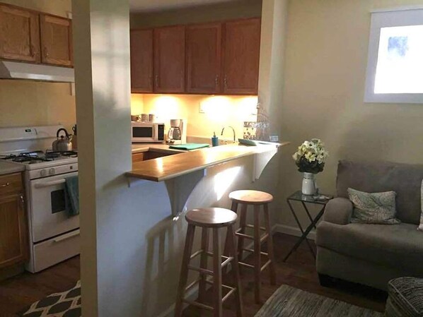 Una cocina compacta con armarios de madera, una estufa y un microondas. Hay dos taburetes cerca de la isla de la cocina.