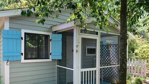 Una casa pequeña con un porche, una puerta con mosquitero y una ventana con contraventanas.