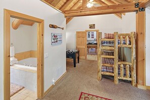 Een kamer met een houten plafond, een tafelvoetbaltafel, een biljarttafel en een houten stoel met ruitkussens.