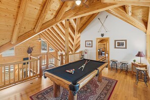 Een houten interieur met een pooltafel, een balkon en een eethoek.