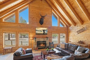 A log cabin interior with a fireplace, leather furniture, and a mounted deer head.