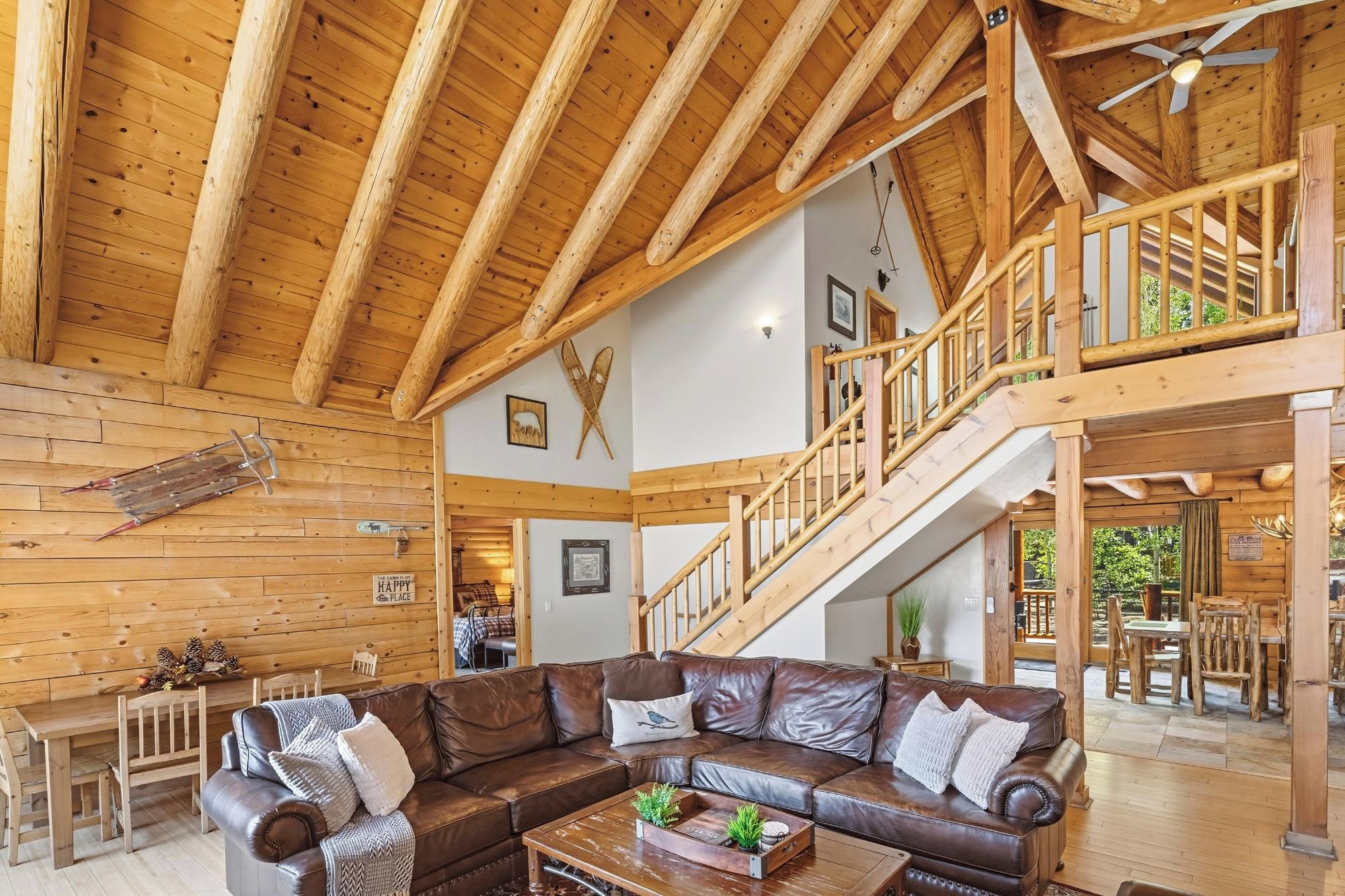 A spacious living area with a high wooden ceiling, a leather sofa, a dining table, and a staircase leading to an upper level.