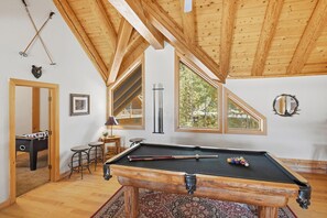 Une pièce dotée d’une table de billard, de poutres en bois au plafond et de grandes fenêtres.