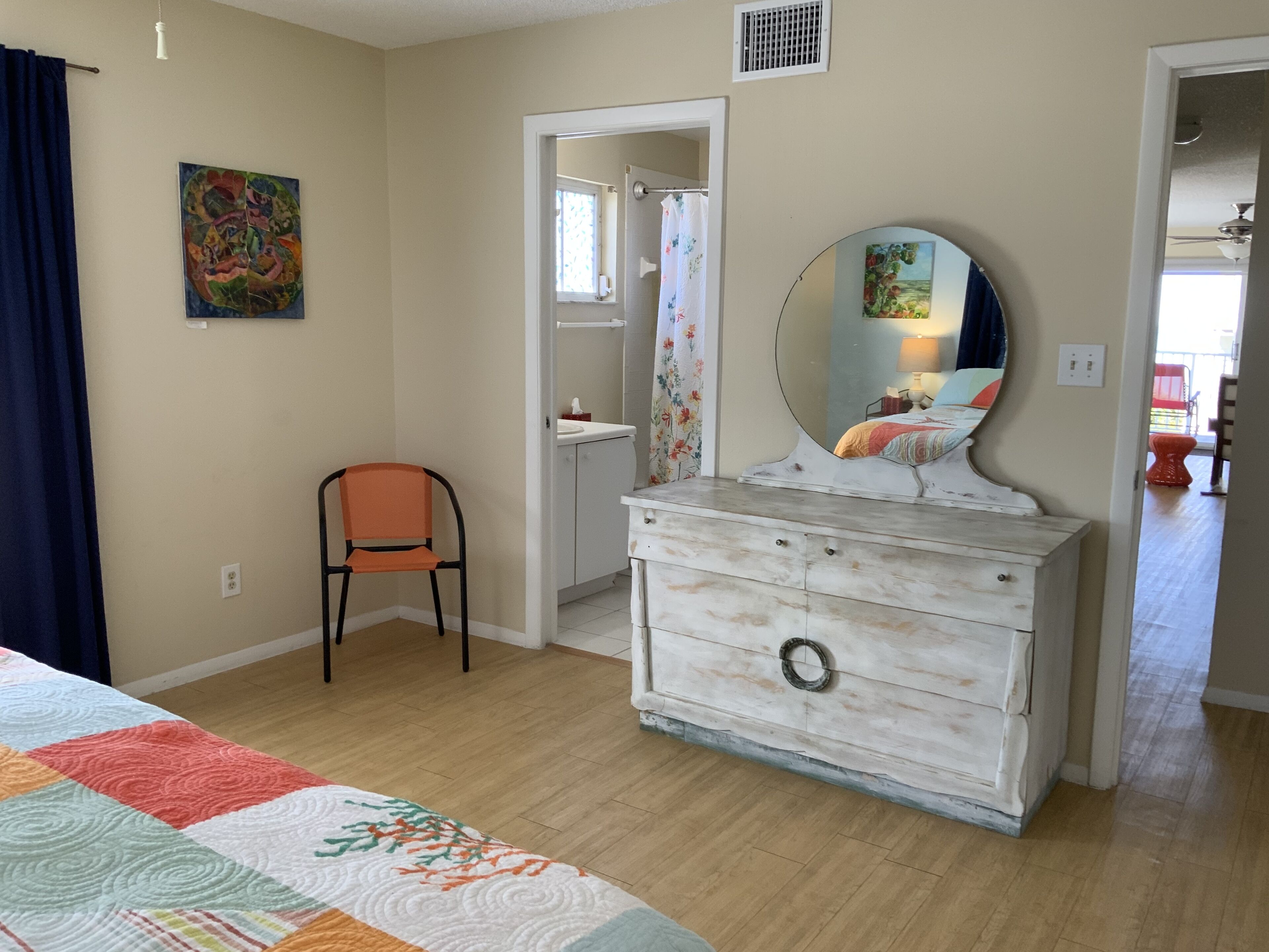 A bedroom with a bed, a dresser, a chair, and a door leading to another room.