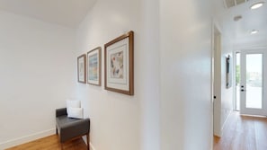 A hallway with a bench, three framed artworks on the wall, and a door leading to another room.