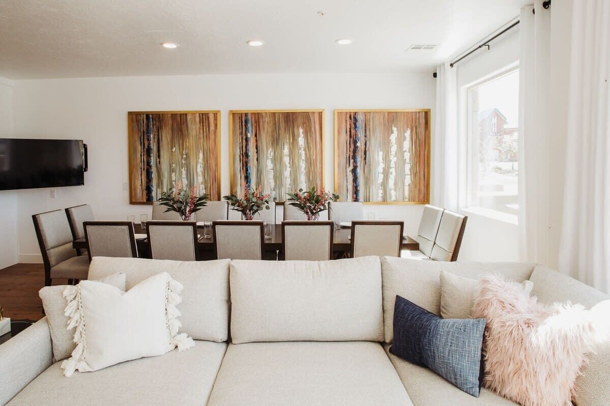 A modern living room with a sectional sofa, a dining area with a table and chairs, and a large window with curtains.