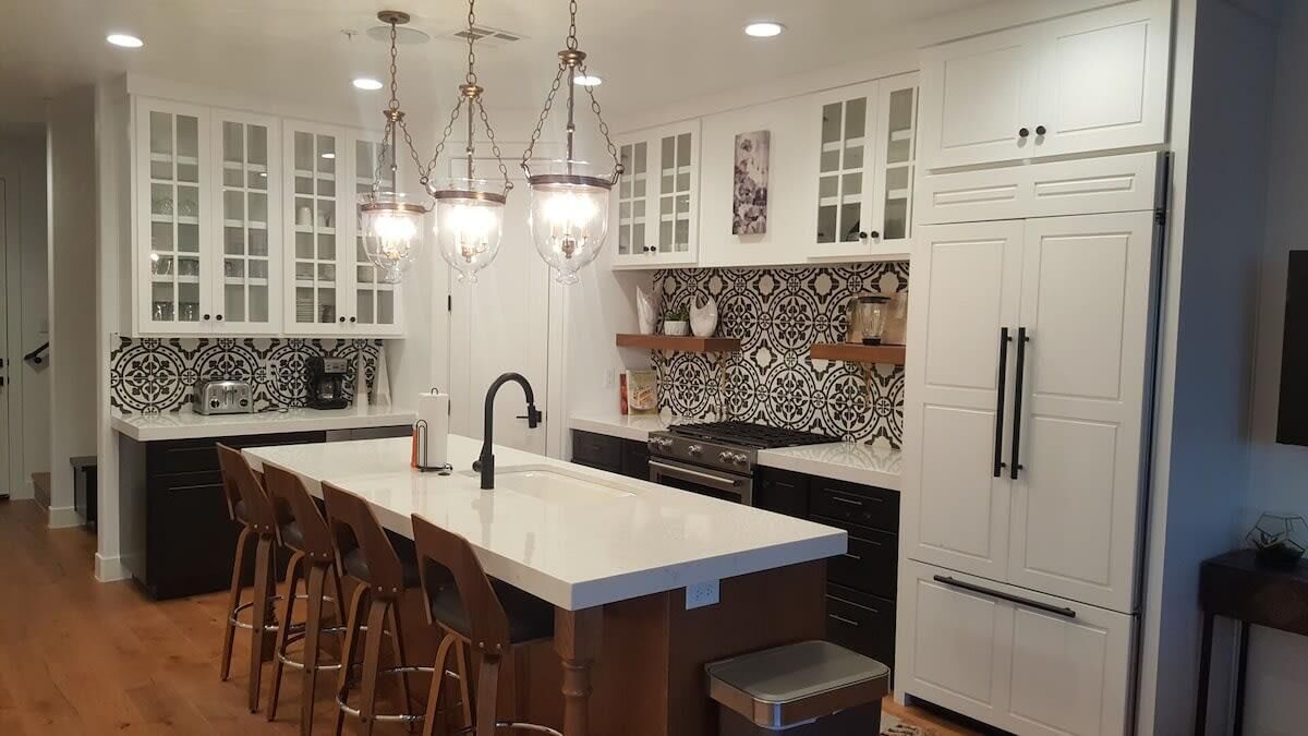 A modern kitchen with white cabinetry, a central island with bar stools, a double oven, and pendant lighting.