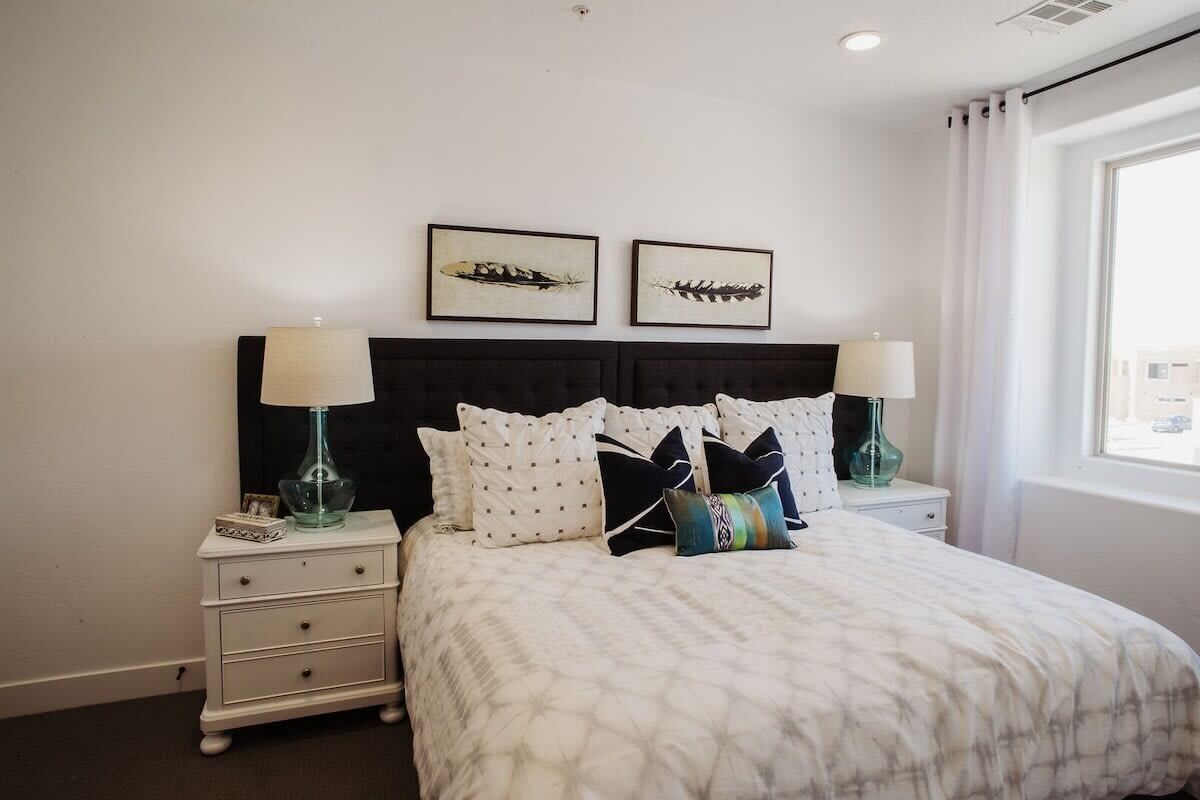 A hotel room with a bed, two nightstands, a window, and two wall-mounted pictures.