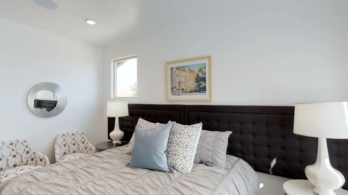 A bedroom with a large bed, two bedside tables, a round mirror, and a framed picture on the wall.