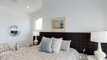 A bedroom with a large bed, two bedside tables, a round mirror, and a framed picture on the wall.