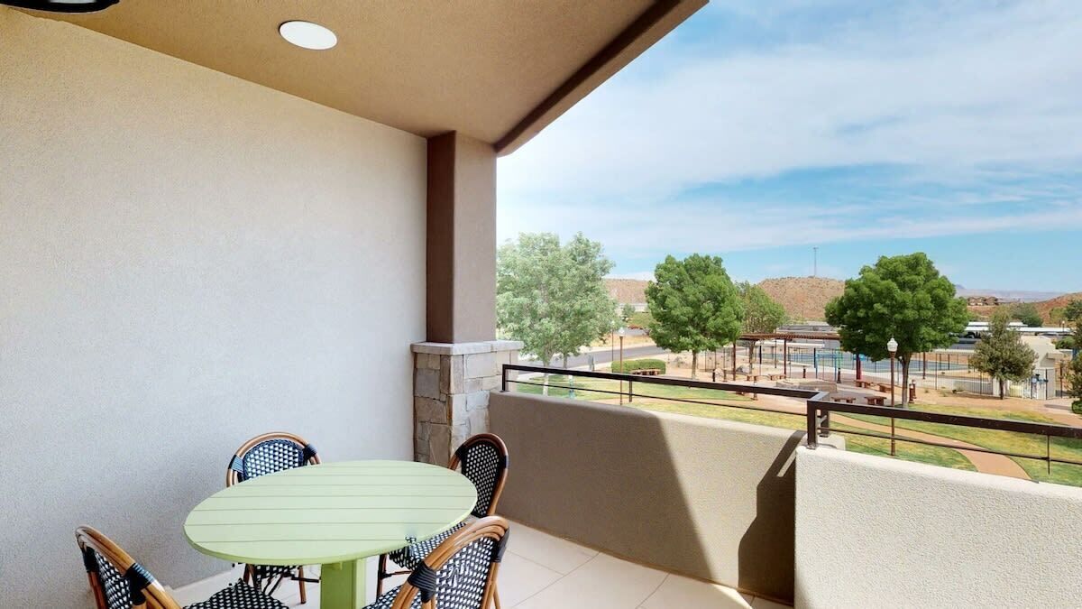 A balcony with a table and chairs, overlooking a park with trees and a distant view of a building.