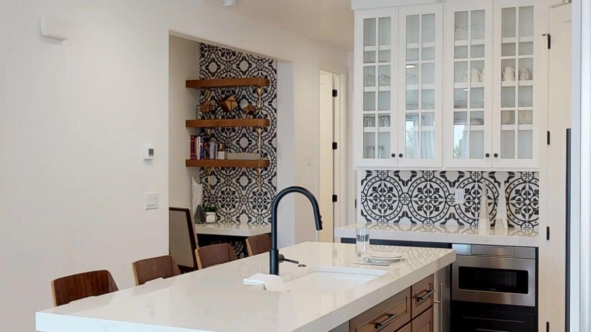 A modern kitchen with a white countertop, black and white patterned backsplash, and built-in cabinets.