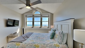 A bedroom with a bed, a ceiling fan, a window with a view, a bedside table, and a TV mounted on the wall. - Serenity Now | Community Beach Access + Pool! (Topsail Beach)