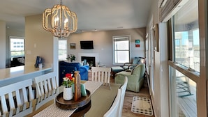 A spacious living room with a high ceiling, a chandelier, a fireplace, and a view of the outside. - Serenity Now | Community Beach Access + Pool! (Topsail Beach)
