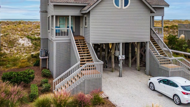 A two-story beach house with a balcony, a staircase leading to the upper floor, and a car parked in front. - Serenity Now | Community Beach Access + Pool! (Topsail Beach)