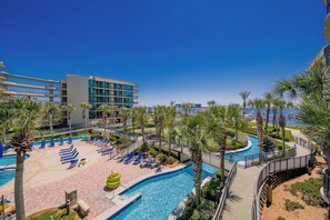 Zwembadgedeelte van een resort met ligbedden, palmbomen en een helder uitzicht op de oceaan.