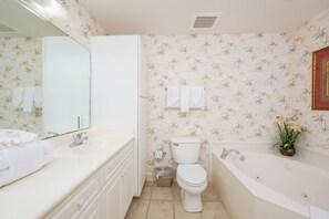 Een badkamer met toilet, wastafel en bad. Handdoeken hangen aan de muur en er staat een prullenbak.