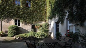A courtyard with a wooden table and benches, surrounded by lush greenery and a building with ivy-covered walls. - Doppler's Apartment fully A/C (Prague)
