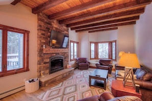 Cozy living room with a stone fireplace, flat-screen TV, and comfortable leather sofas.