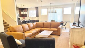 A living room with a sectional sofa, a coffee table, a dark armchair, a dining area with a table and chairs, a kitchen area with cabinets and a countertop, and a staircase. - Entrada 606-Moab Adventure Basecamp (Moab)