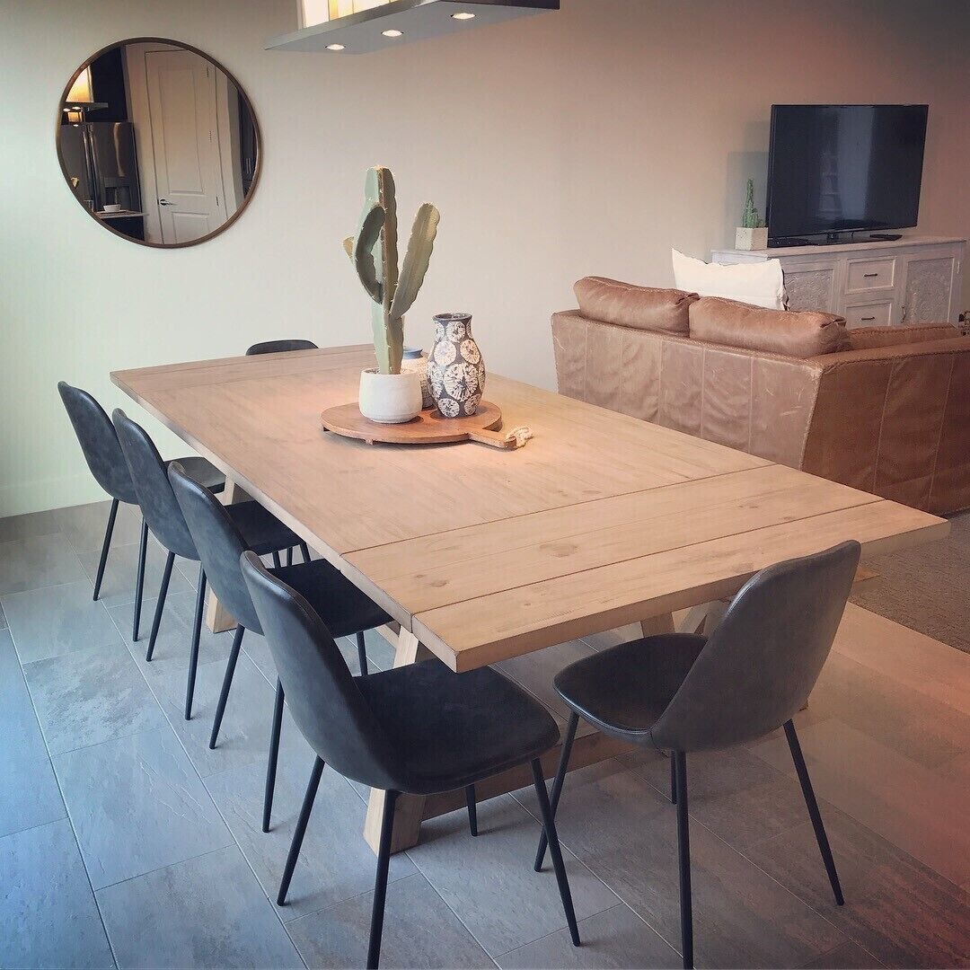 A modern dining area with a wooden table, black chairs, a cactus centerpiece, and a television in the background.