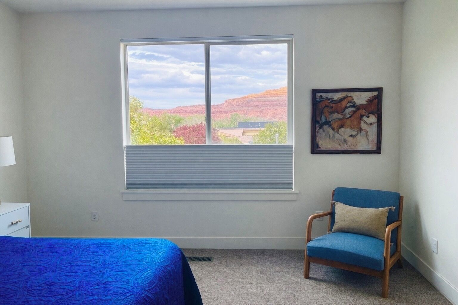 Un dormitorio con cama, una silla, un ventanal con persianas y un cuadro en la pared.