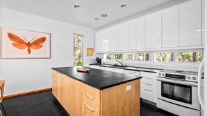 A modern kitchen with white cabinets, a black countertop island, and a large window. - Unique Home in Dauphin Island's Maritime Forest - Stunning Home and Water Views (Dauphin Island)
