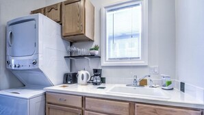 Eine kleine Küche mit Einbauwaschmaschine, Spüle, Holzschränken und einem Fenster mit Jalousien.