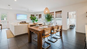 Una sala de estar moderna con una mesa de comedor de madera, asientos cómodos, un televisor grande y vistas al exterior.