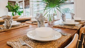 Una mesa de comedor dispuesta con platos, tazones y cubiertos blancos sobre individuales tejidos.
