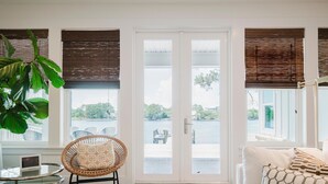 Una habitación con una mesa de vidrio, una silla de mimbre, un sofá blanco y vistas a una masa de agua a través de puertas de vidrio grandes.