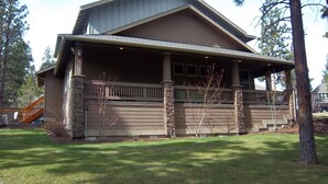 A two-story house with a covered porch, stone pillars, and a wooden deck. - Skyline Lodge, Gorgeous Setting, Walk to Downtown! (Bend)